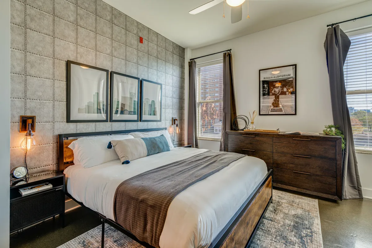 A serene bedroom with a plush bed, tasteful artwork above the headboard, a dressing table, and a window letting in soft morning light. The space feels calm and inviting, perfect for rest and relaxation.