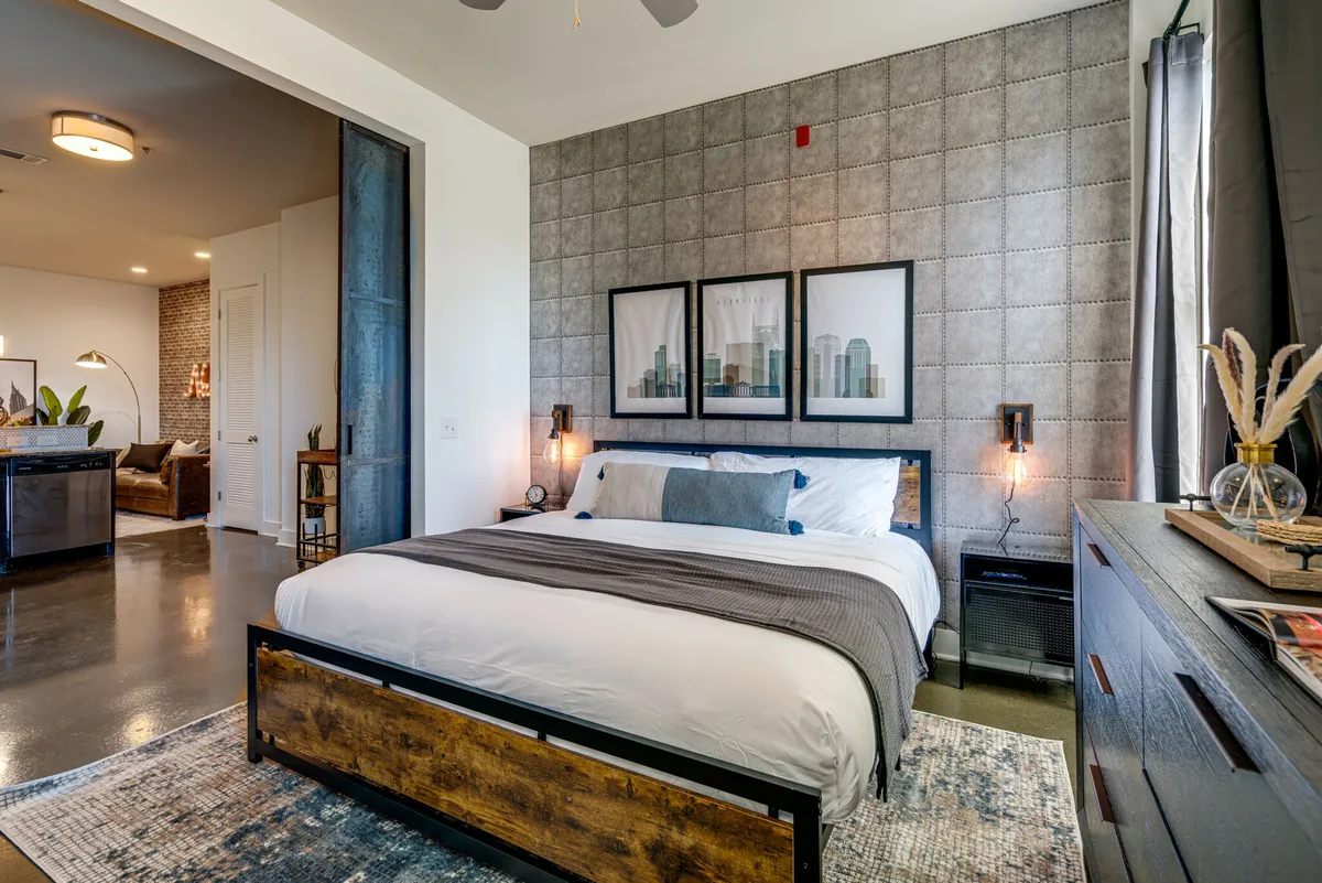 A stylish bedroom with patterned bedding, artwork, nightstands with lamps, and a cozy rug. The space exudes warmth and comfort, ideal for restful nights or lounging with a book.