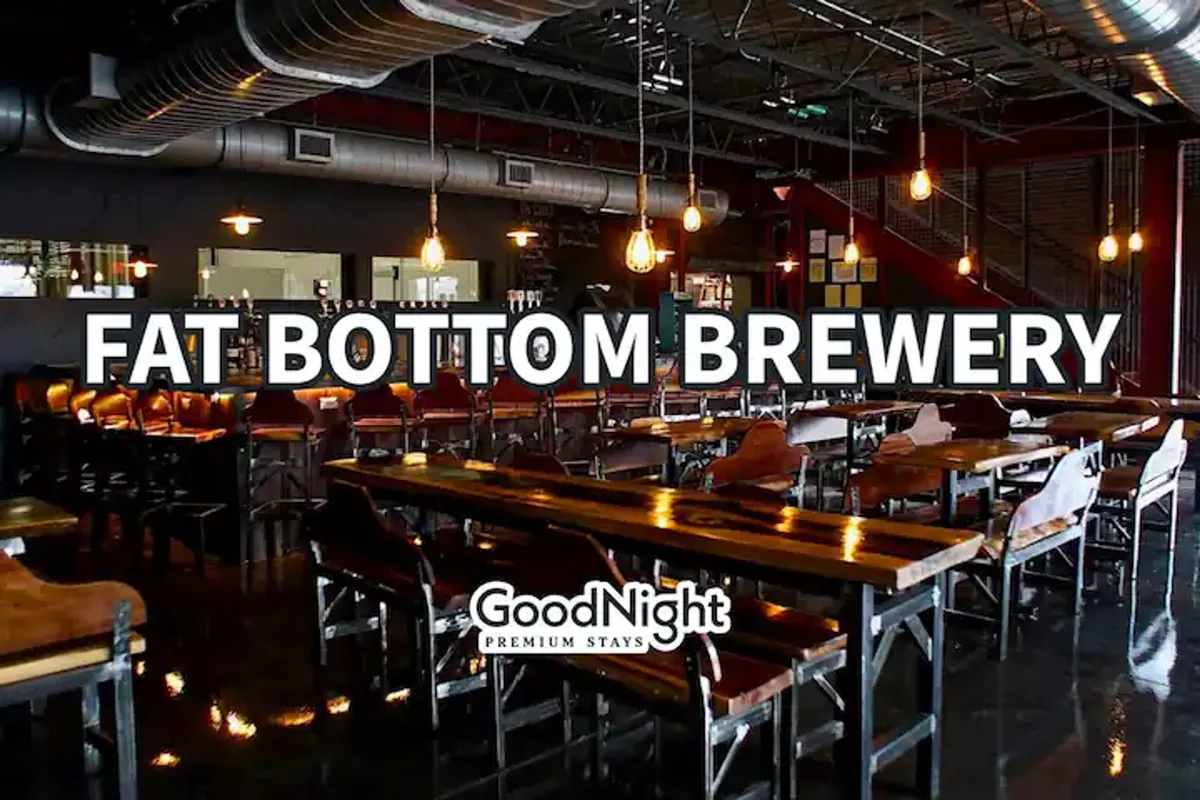 An inviting interior scene showcasing a long communal table and a stylish bar area, ideal for gathering with friends to enjoy craft beers, meals, or conversations. The hanging light fixtures and warm ambiance suggest a lively, sociable vibe.